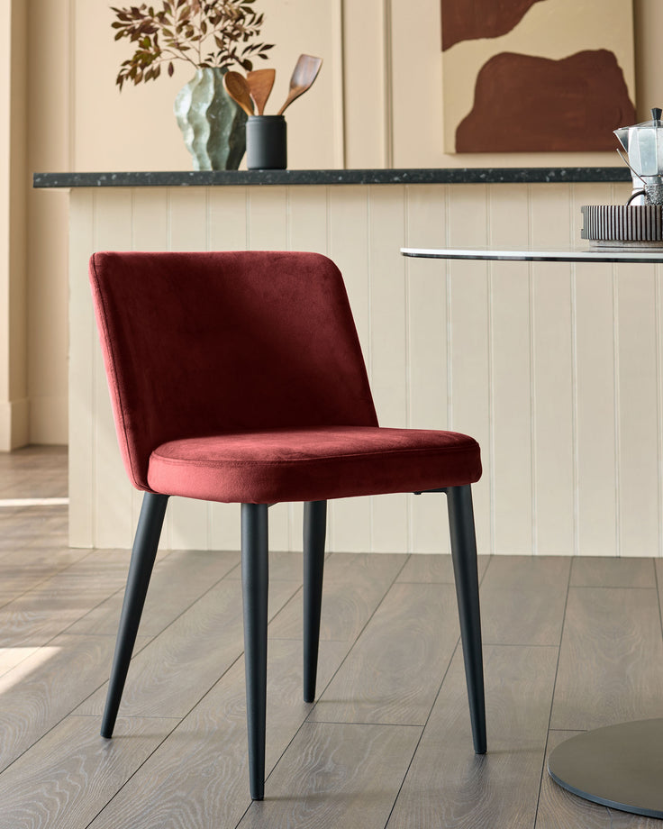 A stylish red velvet chair with sleek black legs sits elegantly by a table.