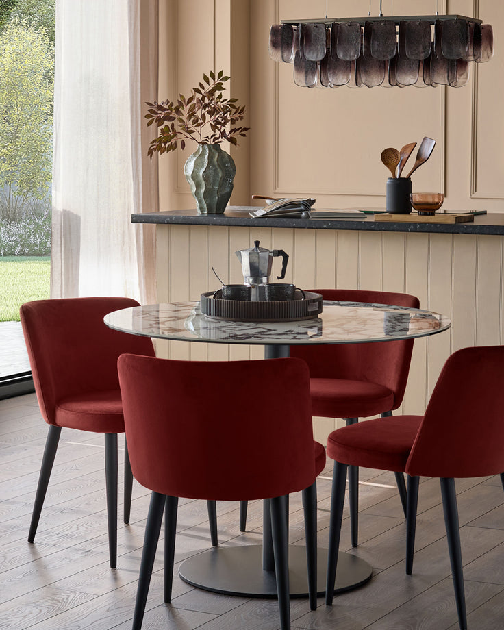 A round marble table with four stylish red velvet chairs. Modern dining furniture for the contemporary home.