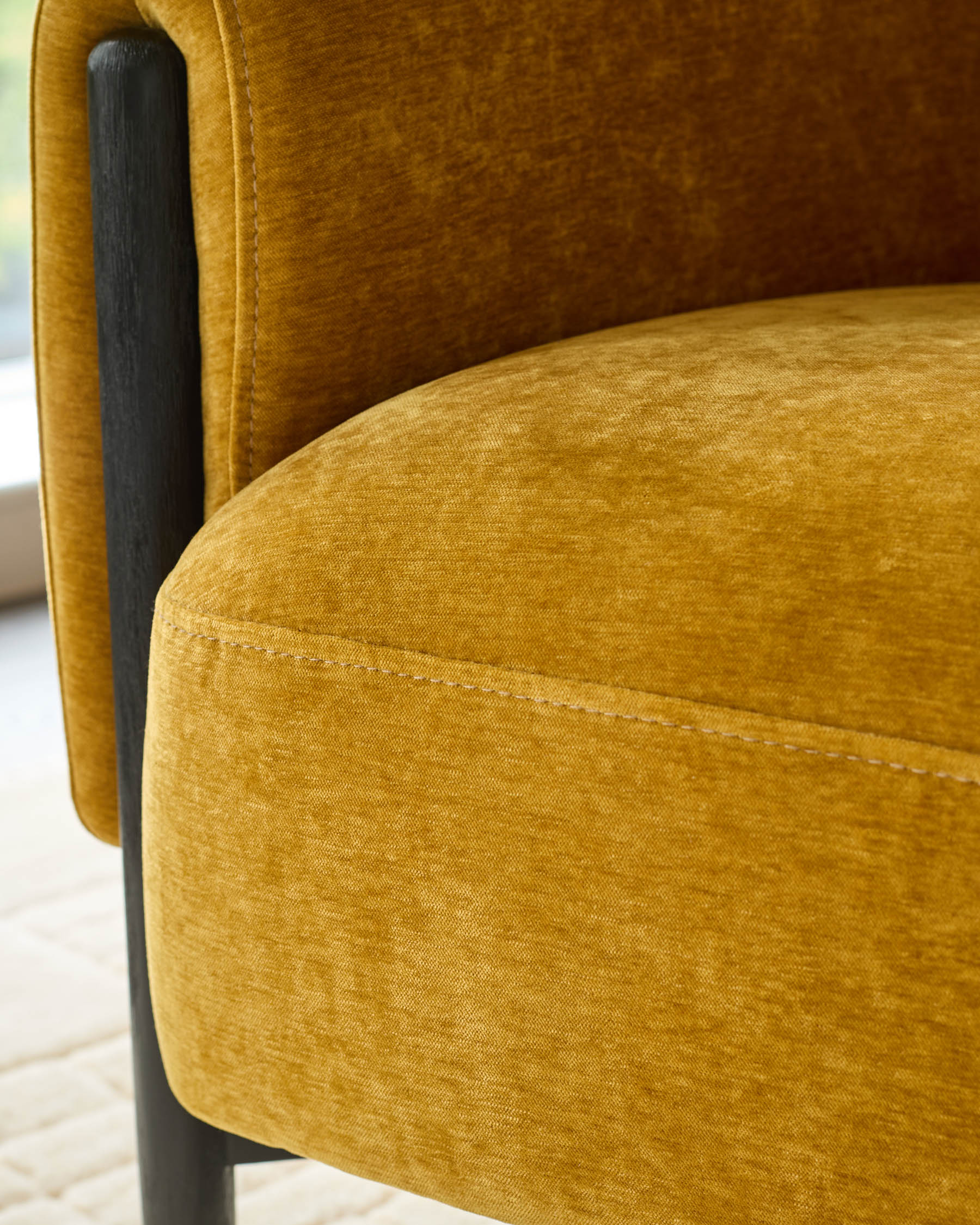Close-up of a mustard yellow upholstered armchair with dark wooden legs. Comfortable and stylish seating.