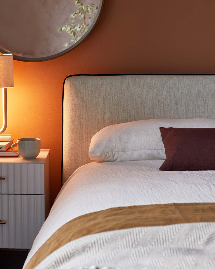 A bedroom scene shows a neutral headboard, a white bedside table, soft lamp light, and pops of colour.