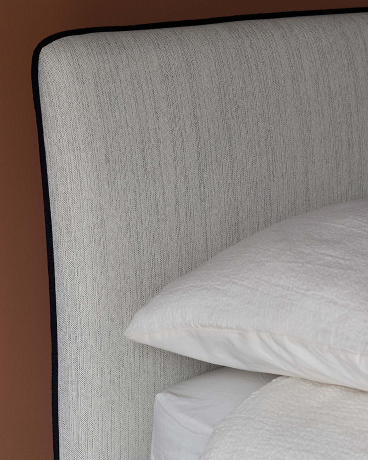 Close-up of a stylish bed headboard with textured fabric and a crisp white pillow and duvet cover.