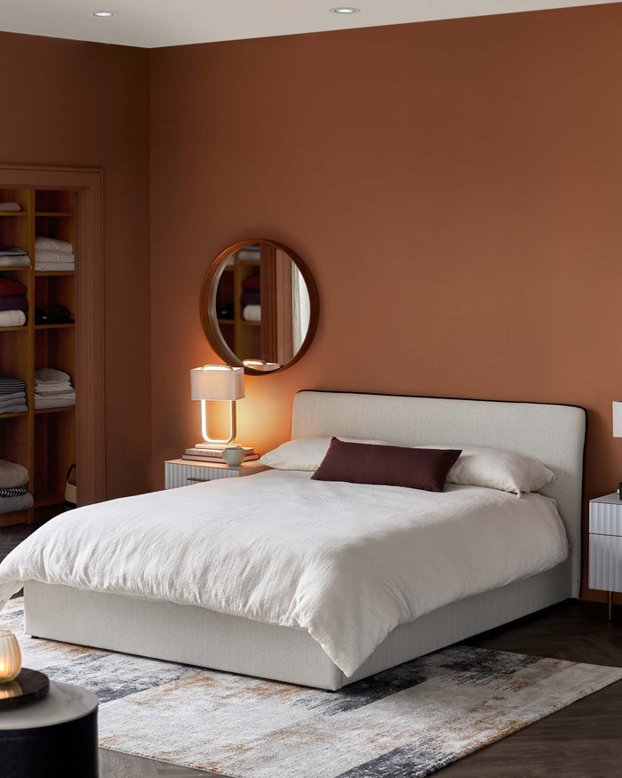 Bedroom with a stylish bed, bedside tables, and a round mirror. A neutral rug adds a touch of texture.