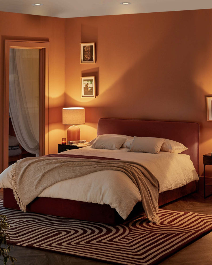 A stylish bedroom with a red bed, bedside table and a patterned rug creates a warm, inviting space.