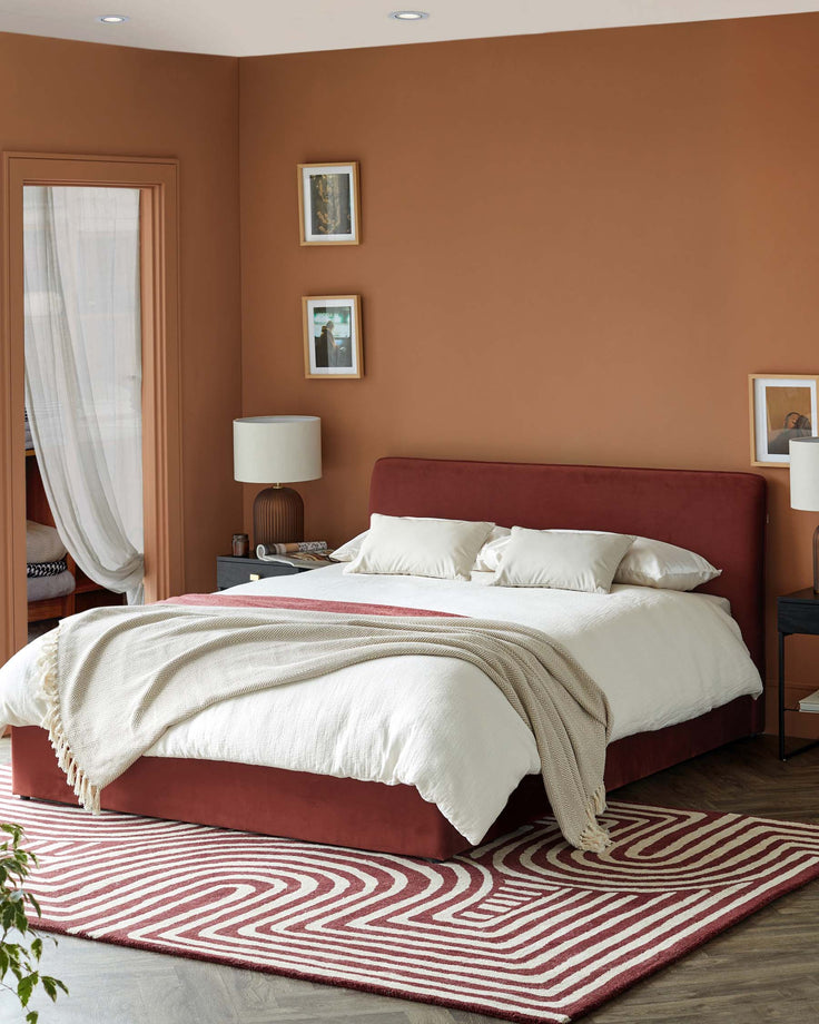 A stylish bedroom with a red bed, patterned rug, and bedside tables. Comfortable and modern bedroom furniture.