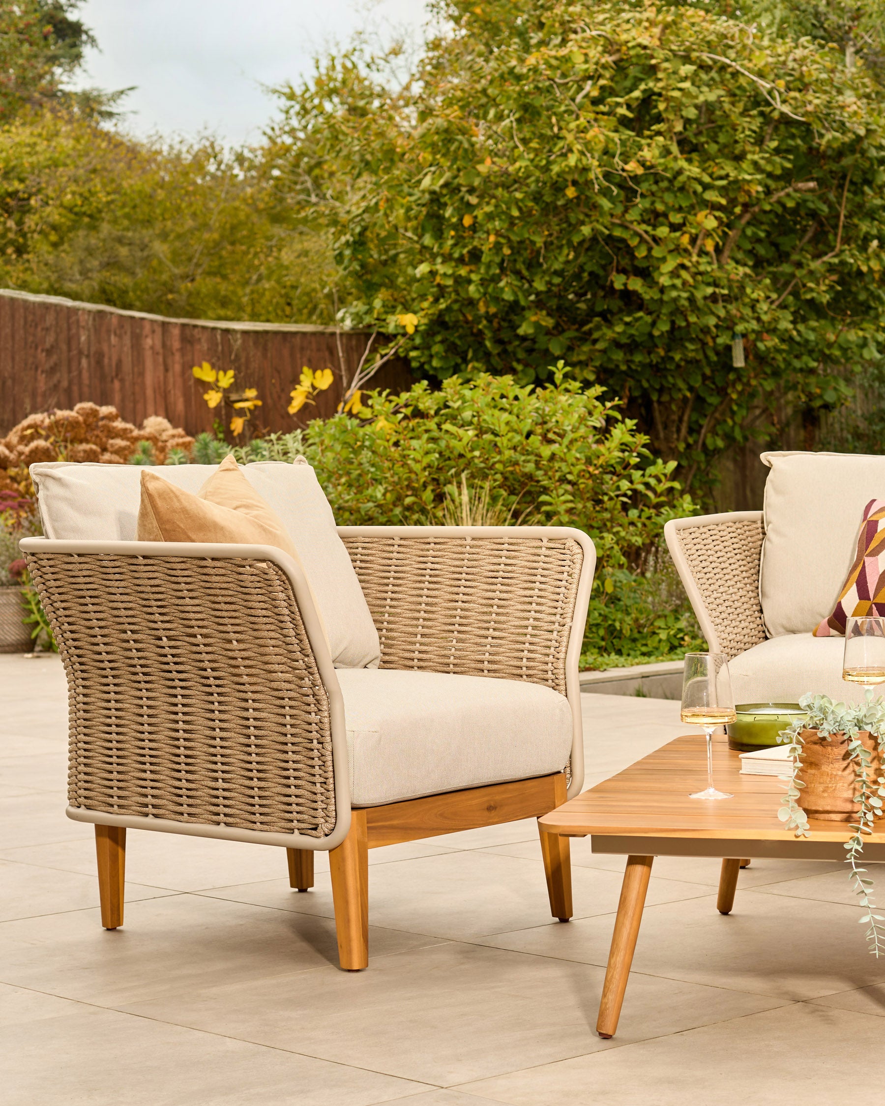 Tuscany garden set with woven rattan armchair, cream cushions, wooden legs, and wooden coffee table on patio.