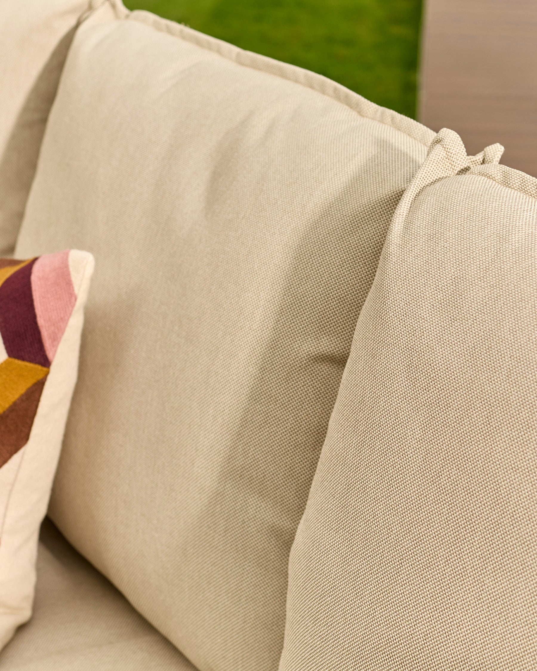 Beige linen upholstered sofa with rolled armrest and decorative pillow detail, close-up view.