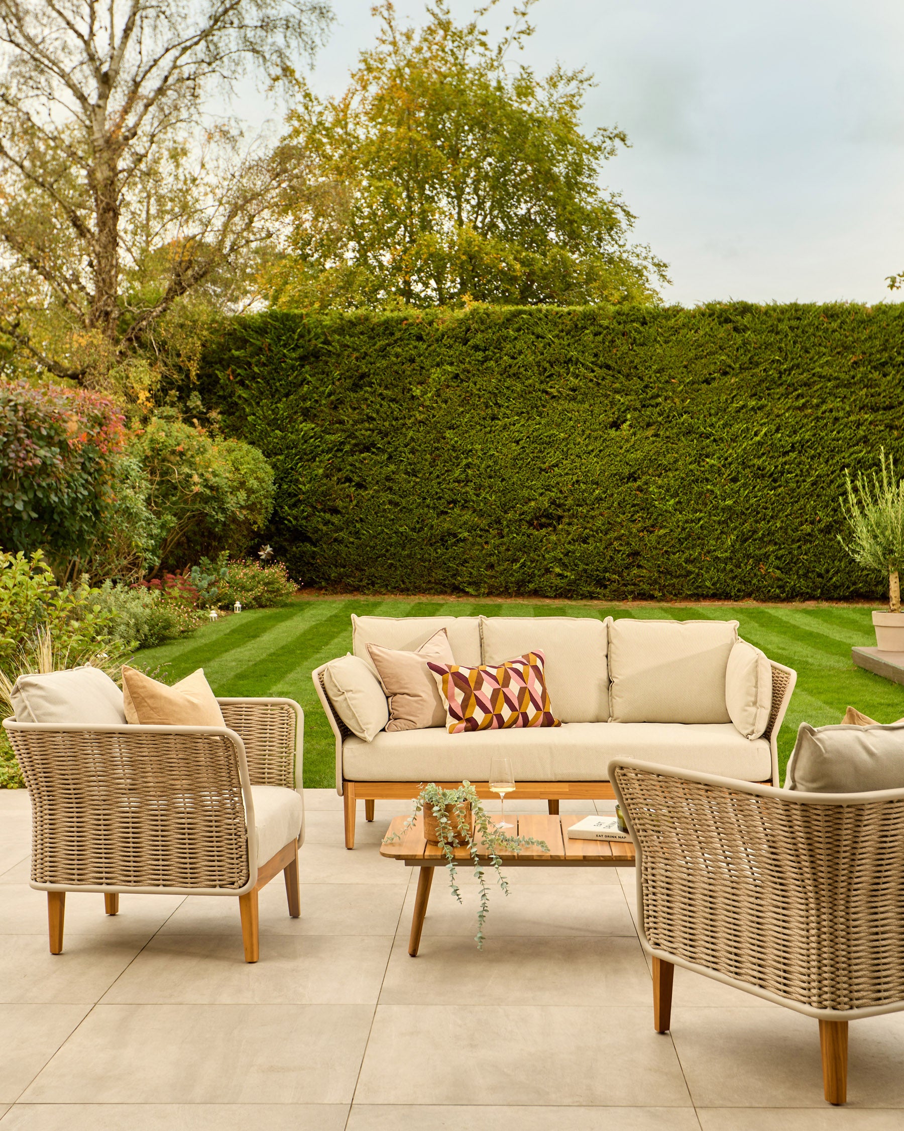 Tuscany garden furniture set with natural woven rattan 3-seater sofa, two armchairs, and wooden coffee table on patio.