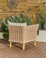 Tuscany garden armchair with natural woven rattan back, cream cushion, and wooden legs, photographed outdoors on a deck.