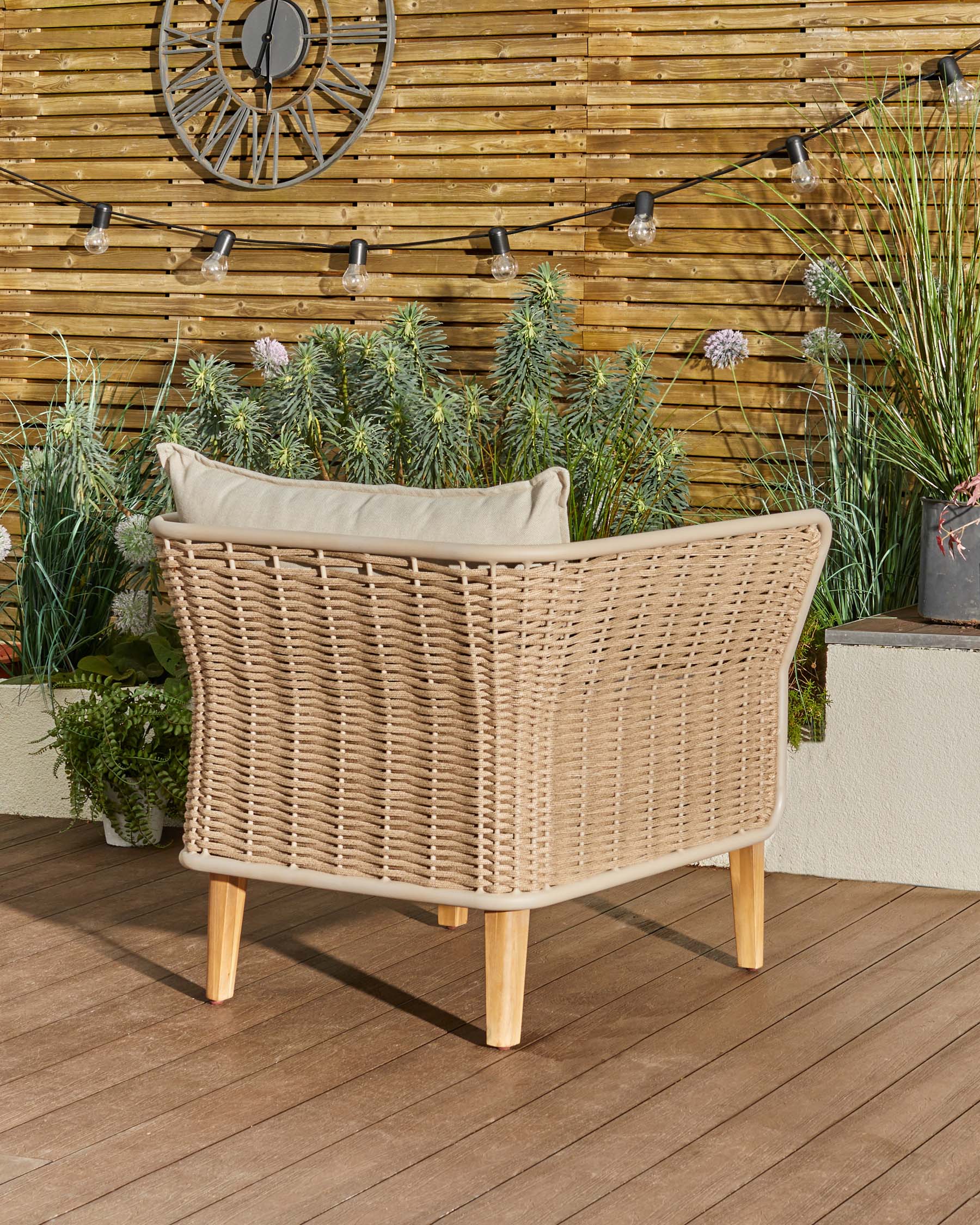 Tuscany garden armchair with natural woven rattan back, cream cushion, and wooden legs, photographed outdoors on a deck.