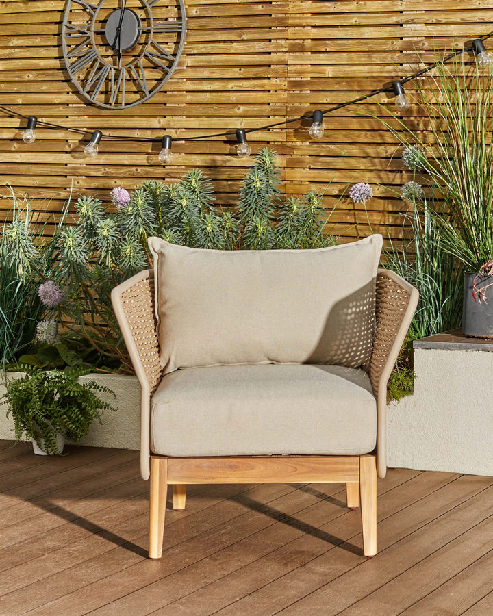 Tuscany garden armchair in natural acacia wood with cream fabric cushions, woven rattan armrests, displayed on wooden deck.