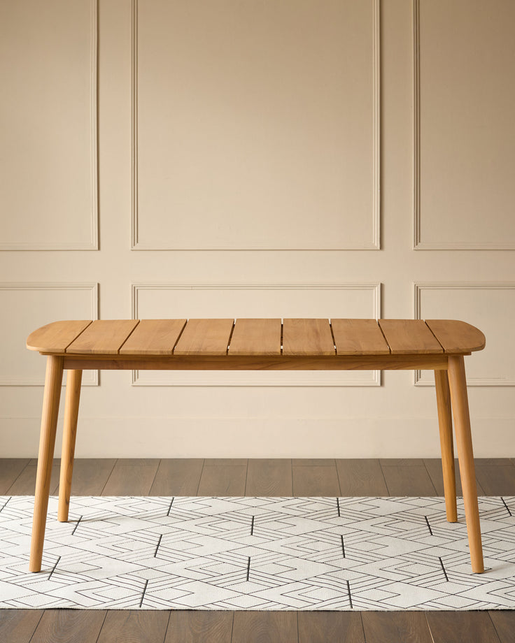 Tuscany Garden teak wood dining table with rounded ends, featuring slatted top and tapered legs in a bright interior space.