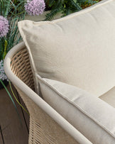 Tuscany garden armchair with natural acacia wood frame and cream fabric seat, angled view showing curved armrest detail.