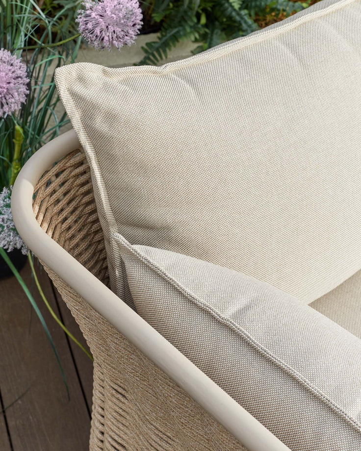 Tuscany garden armchair with natural acacia wood frame and cream fabric seat, angled view showing curved armrest detail.