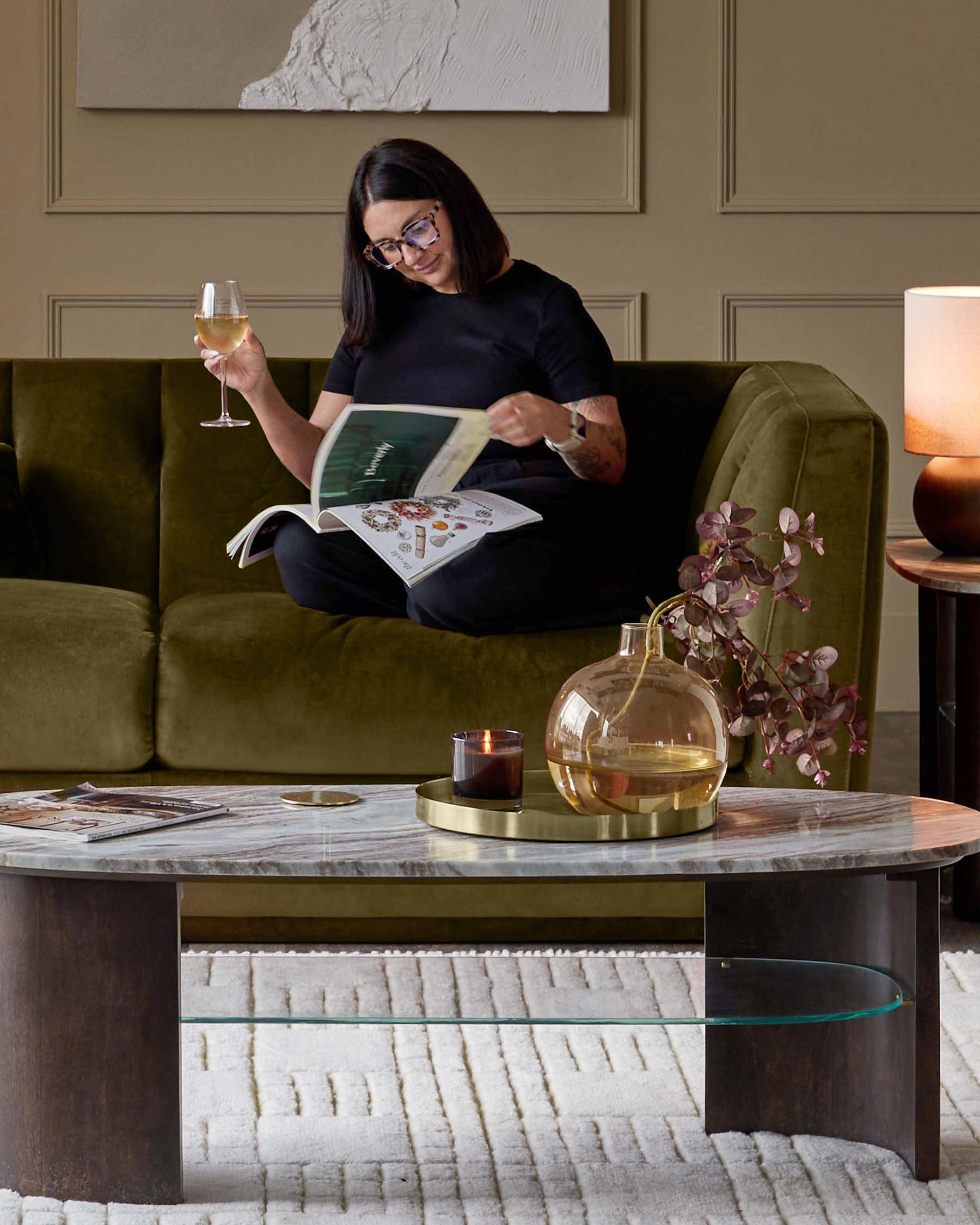 Olive green three-seater velvet sofa styled in a modern living room setting with a woman seated on it.