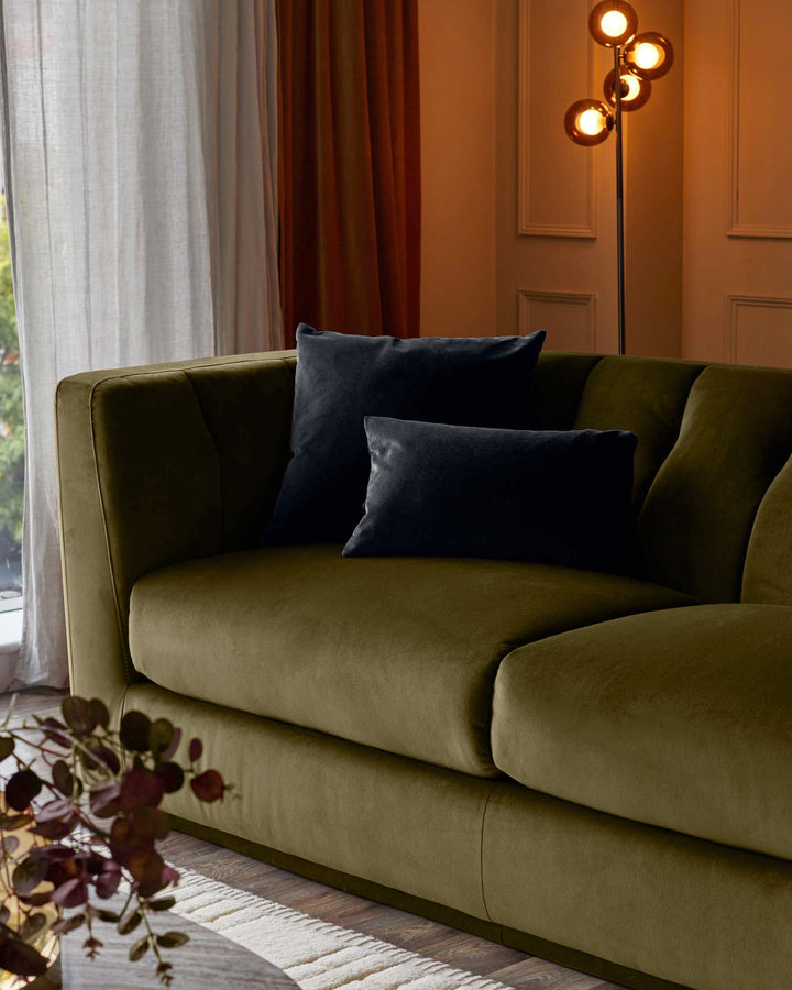 Olive green velvet 2-seater sofa with curved arms and black cushions in a styled living room setting.