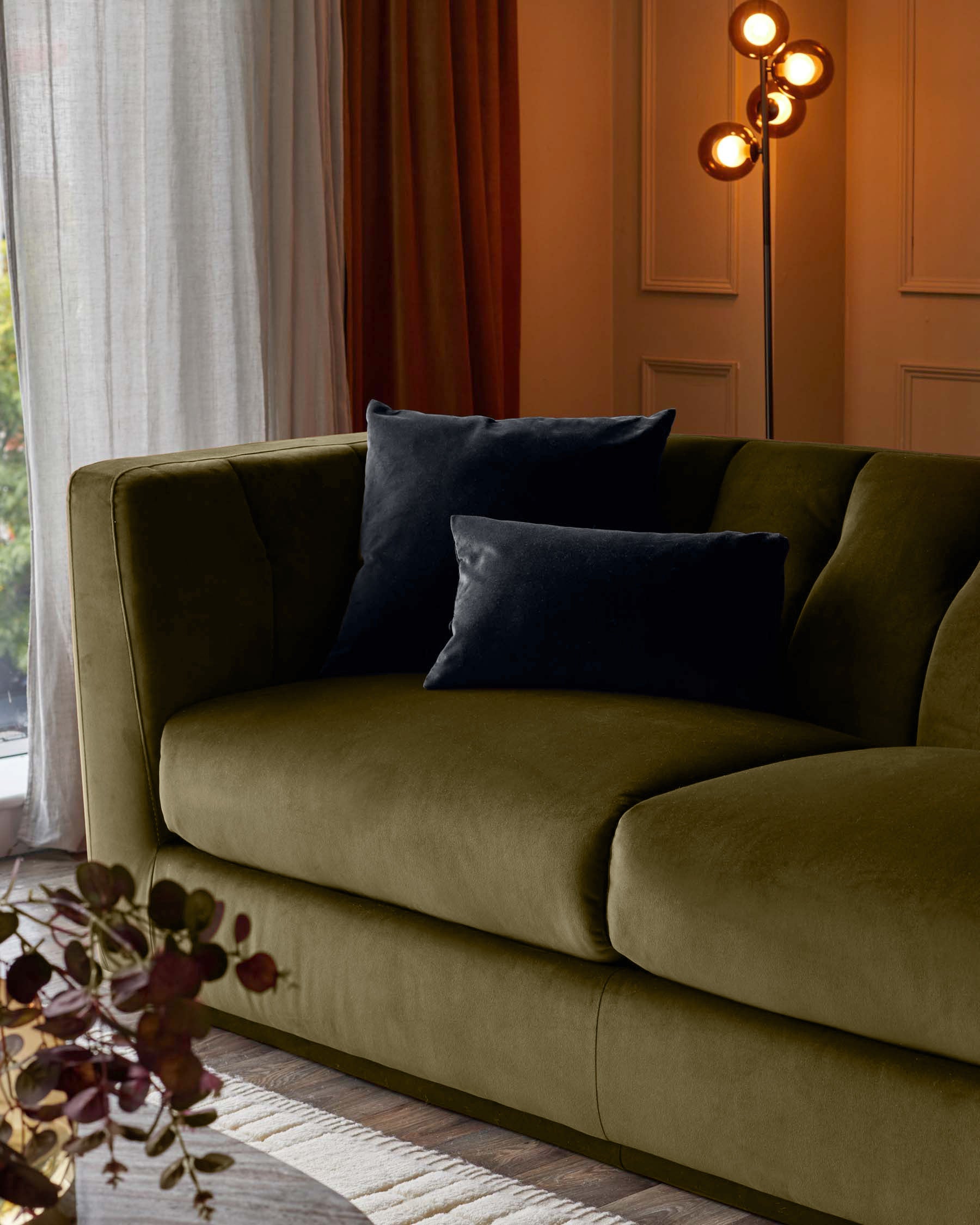 Olive green velvet 3-seater sofa with curved arms and black pillows, styled in a modern living room setting.