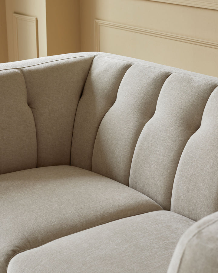 Close-up of a stylish, light beige sofa with a curved back and plush seating, set against a neutral wall.