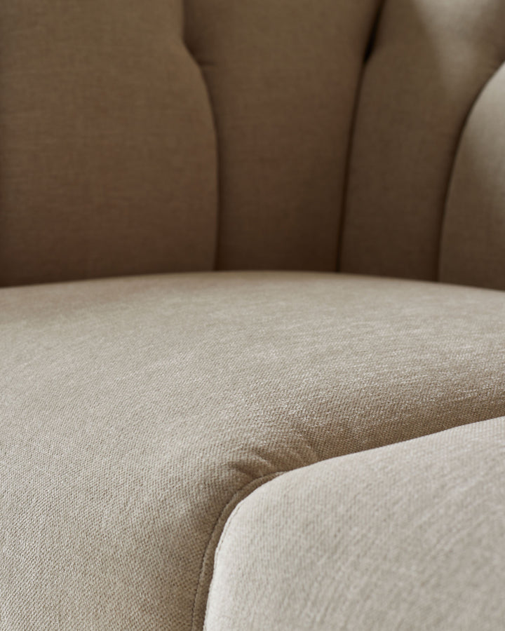 Close-up of a beige sofa with button detailing, showing the texture of the fabric and the curved design of the furniture.