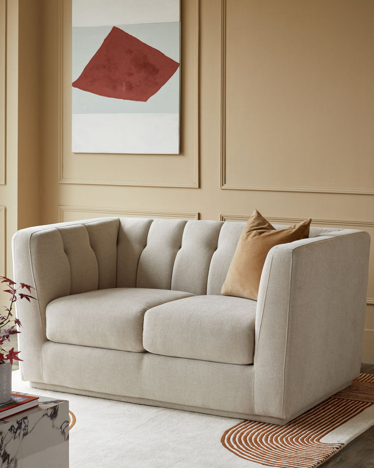 A contemporary loveseat sofa with a tan throw pillow, set against a beige wall with modern art.