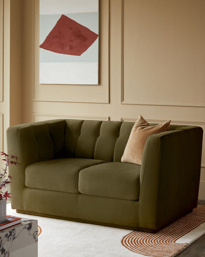 Olive green 2-seater sofa with channeled back and arms, styled with a peach cushion in a contemporary living room setting.