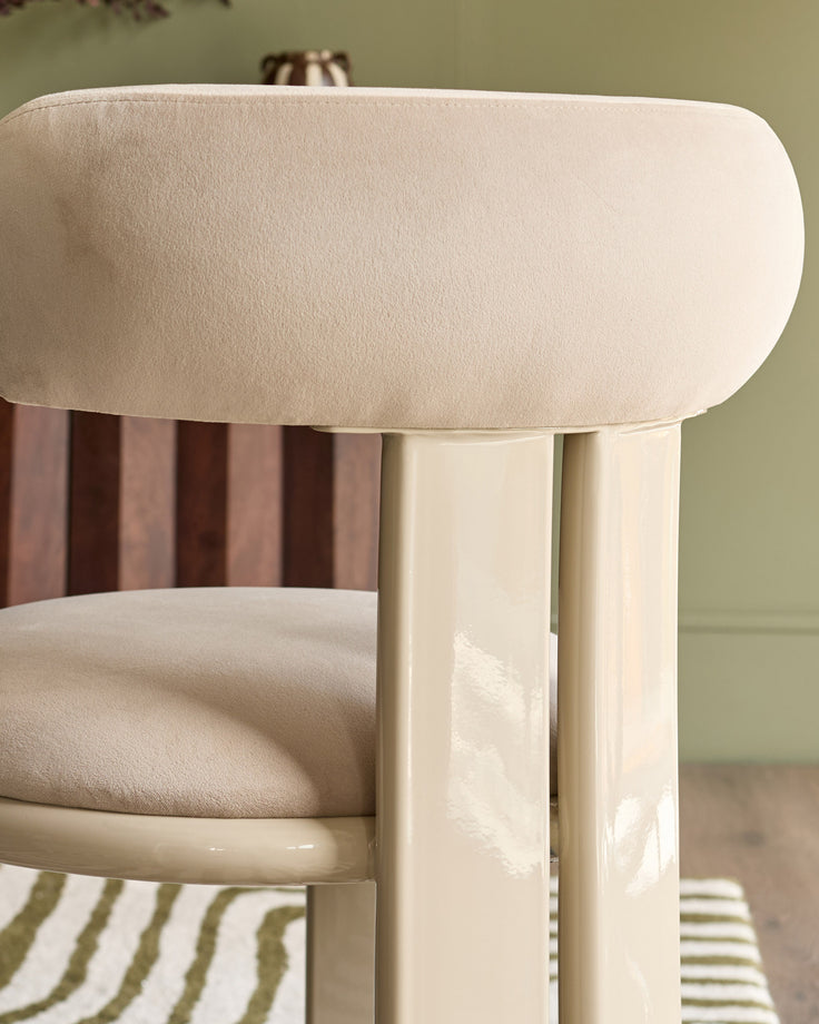 Valerie dining chair in champagne velvet, showcasing curved backrest and cylindrical wooden legs from a side angle.