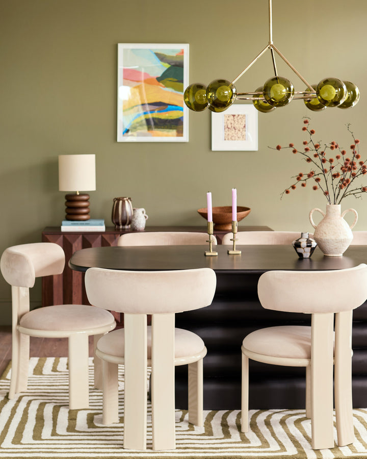 Champagne velvet dining chair with curved backrest and cylindrical legs in a modern dining room setting.