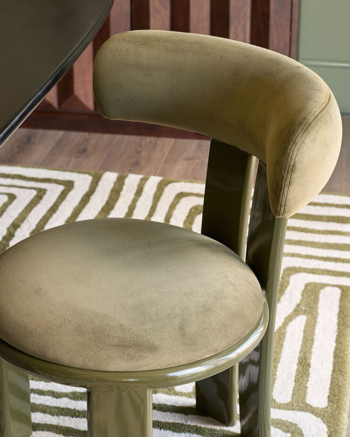 Valerie dining chair in olive green velvet, side view showing curved backrest and round seat on metal base.