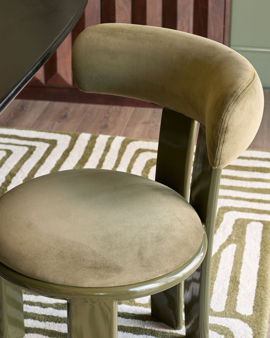 Valerie dining chair in olive green velvet, side view showing curved backrest and round seat on metal base.