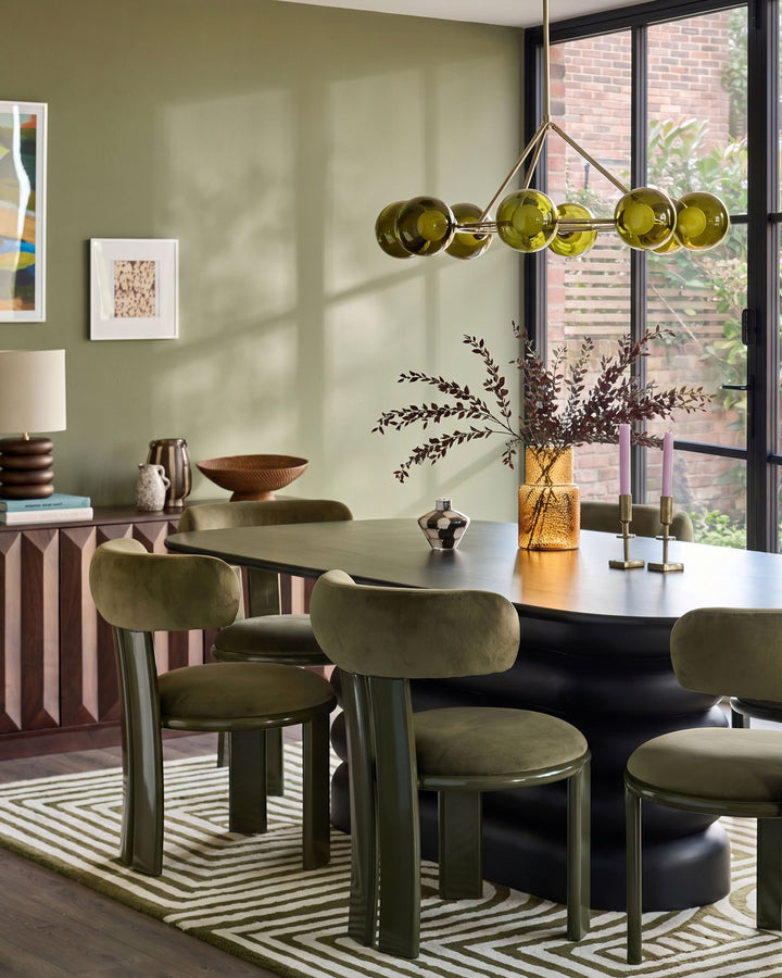 Valerie dining chair in olive green velvet, shown in a modern dining room setting around a black table.