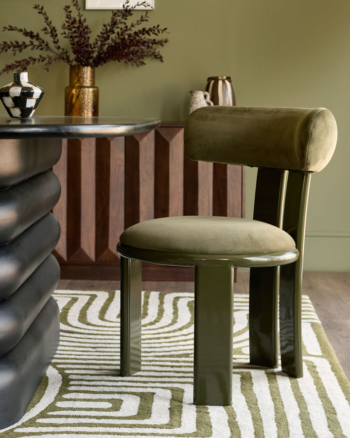 Valerie dining chair in olive green velvet with cylindrical backrest and metal legs, styled in room setting.
