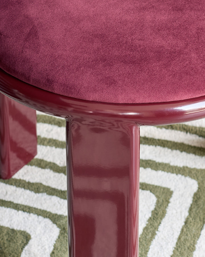 Valerie dining chair in plum velvet, shown from above with glossy burgundy legs on a geometric patterned rug.