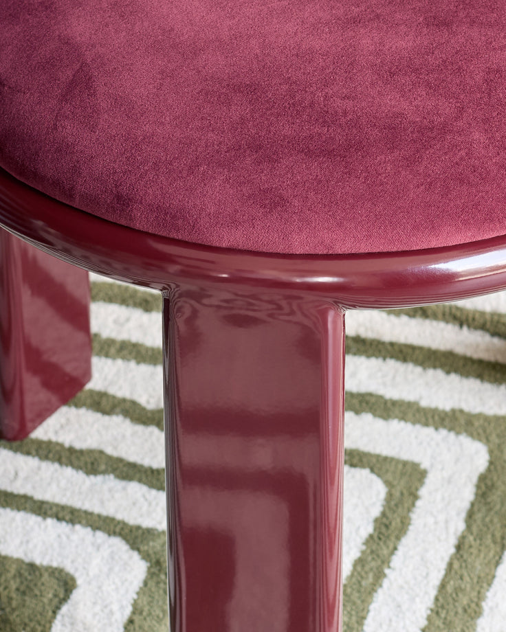 Valerie dining chair in plum velvet, shown from above with glossy burgundy legs on a geometric patterned rug.