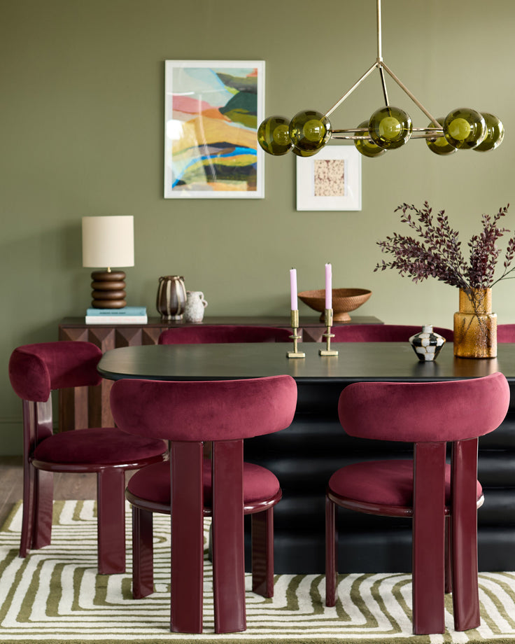 Plum velvet dining chair with curved back and legs, shown in modern dining room setting with black table and sage green walls.