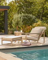 Verano lounge chair with footstool in natural wood and beige cushions, poolside setting with garden backdrop.