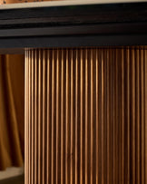 Close-up of natural wood grain detail on Vidal dining table edge, showing vertical fluted texture and warm honey-brown finish.