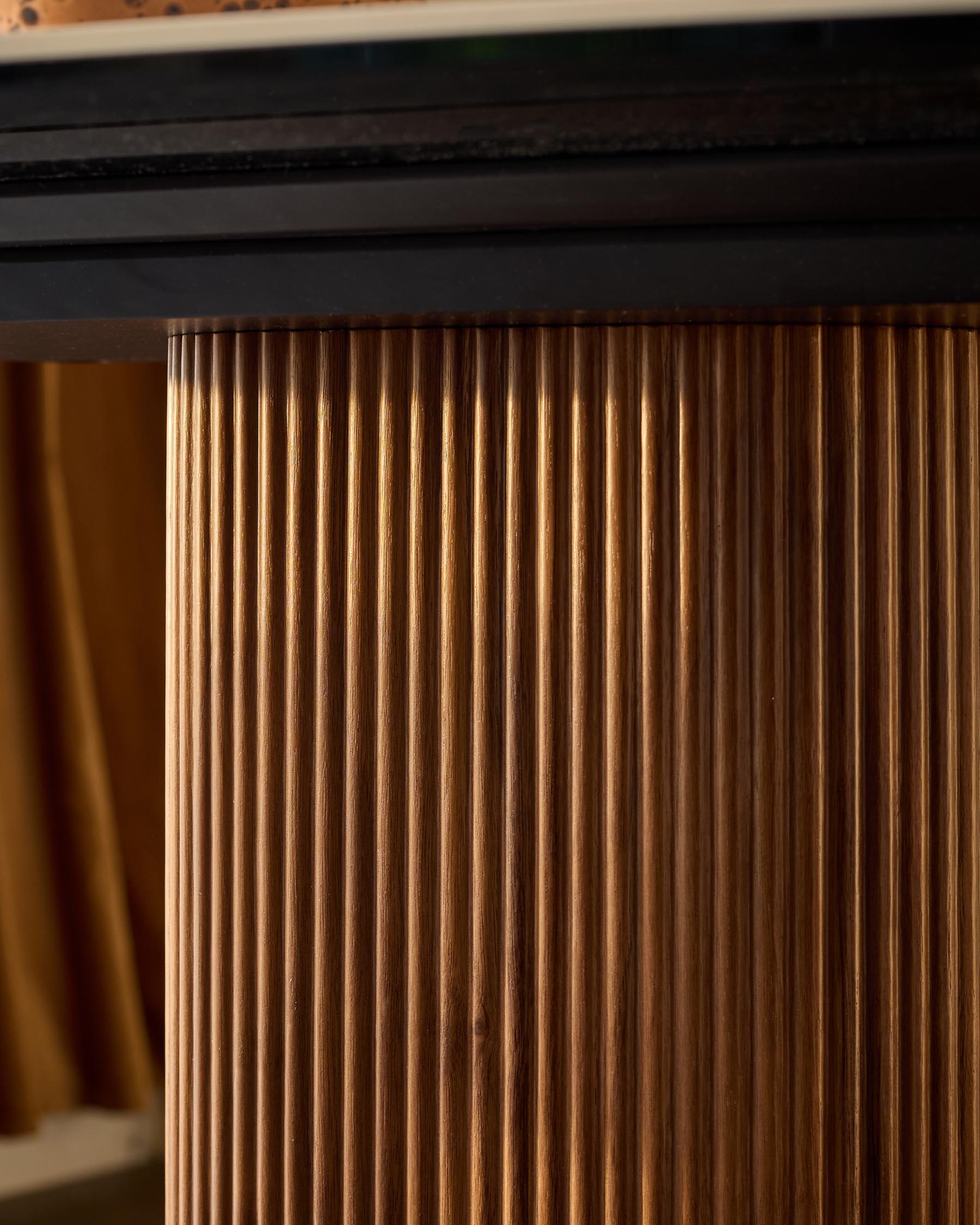 Close-up of natural wood grain detail on Vidal dining table edge, showing vertical fluted texture and warm honey-brown finish.