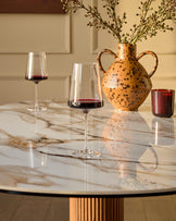 Vidal 6-seater dining table in natural ceramic with marble-effect top and fluted wood pedestal base, styled with wine glasses and decorative vase.