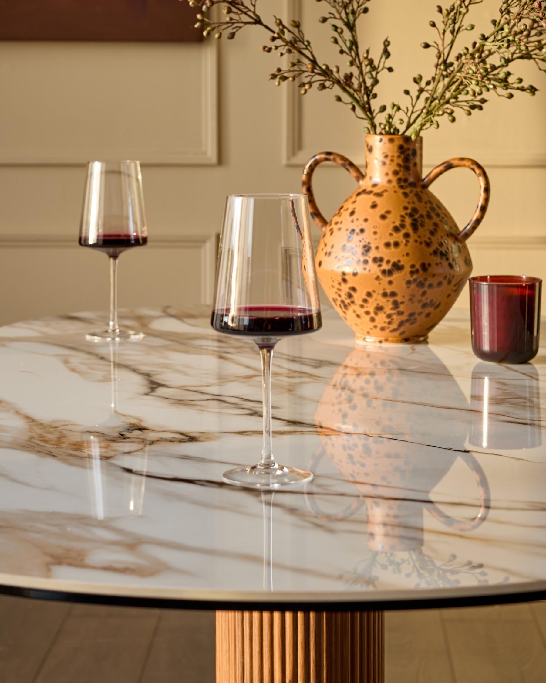 Vidal 6-seater dining table in natural ceramic with marble-effect top and fluted wood pedestal base, styled with wine glasses and decorative vase.