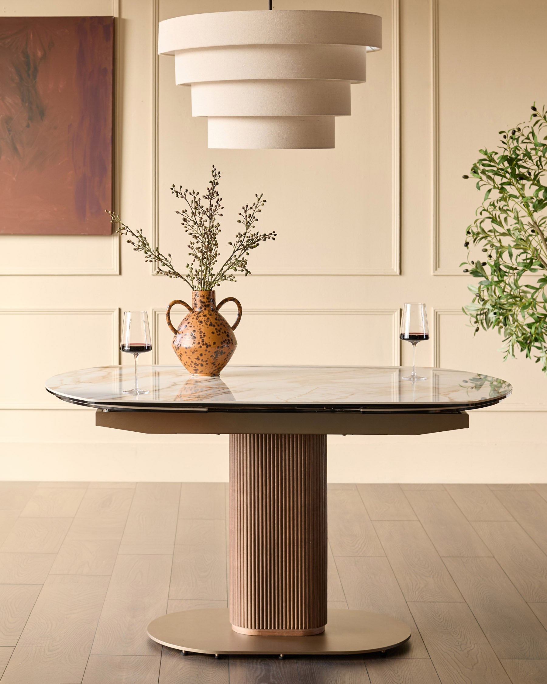 Vidal extending dining table in natural finish with round marble top, vertical ribbed pedestal base, and two wine glasses displayed.