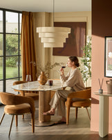Vidal round dining table in natural ceramic with fluted wood base, shown in a warm, modern dining space with matching chairs.