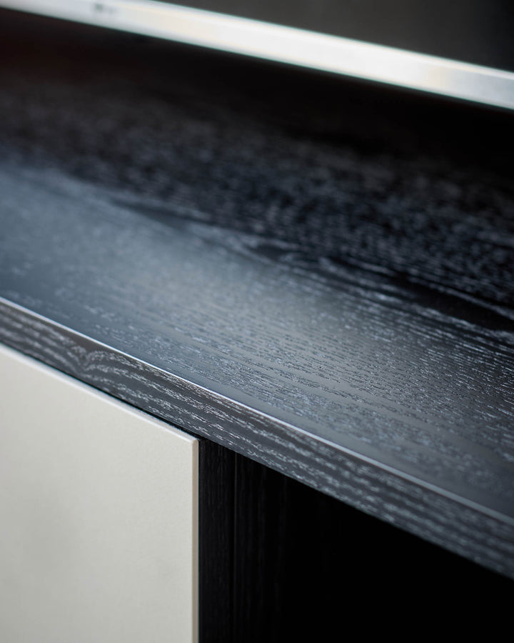 Dark wood TV unit edge detail showing textured finish and white trim accent against white base.