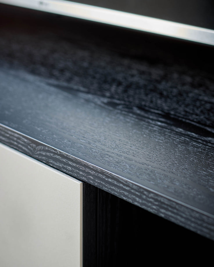 Dark wood TV unit edge detail showing textured finish and white trim accent against white base.