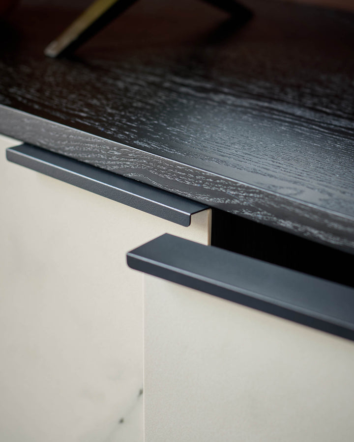 Dark charcoal handle detail on Winslow TV unit with cream base and black wood-grain top surface.