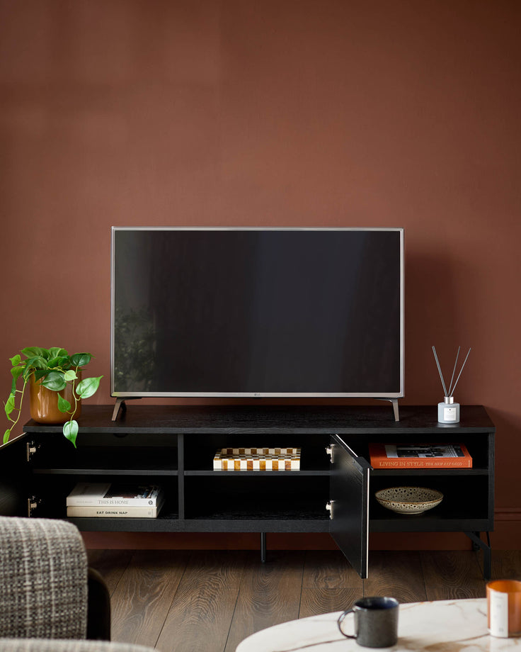 Black TV unit with open shelving, brass handles, and angled wooden legs, styled in a living room setting.