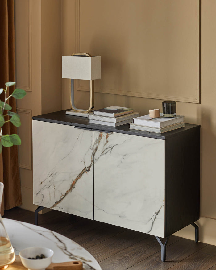 A dark wood and faux marble sideboard with a lamp and books on top.