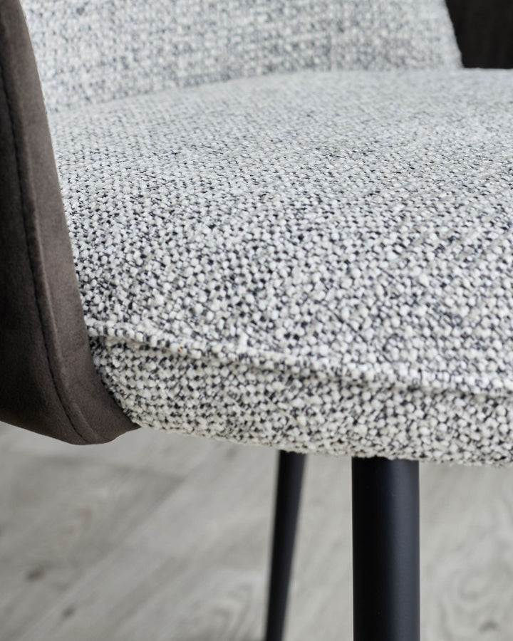 A close up of a stylish chair upholstered in a textured brown fabric with dark brown arm rests and legs.