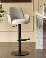 Wren gas lift bar stool in natural fabric with black metal base, shown in kitchen setting next to marble countertop.