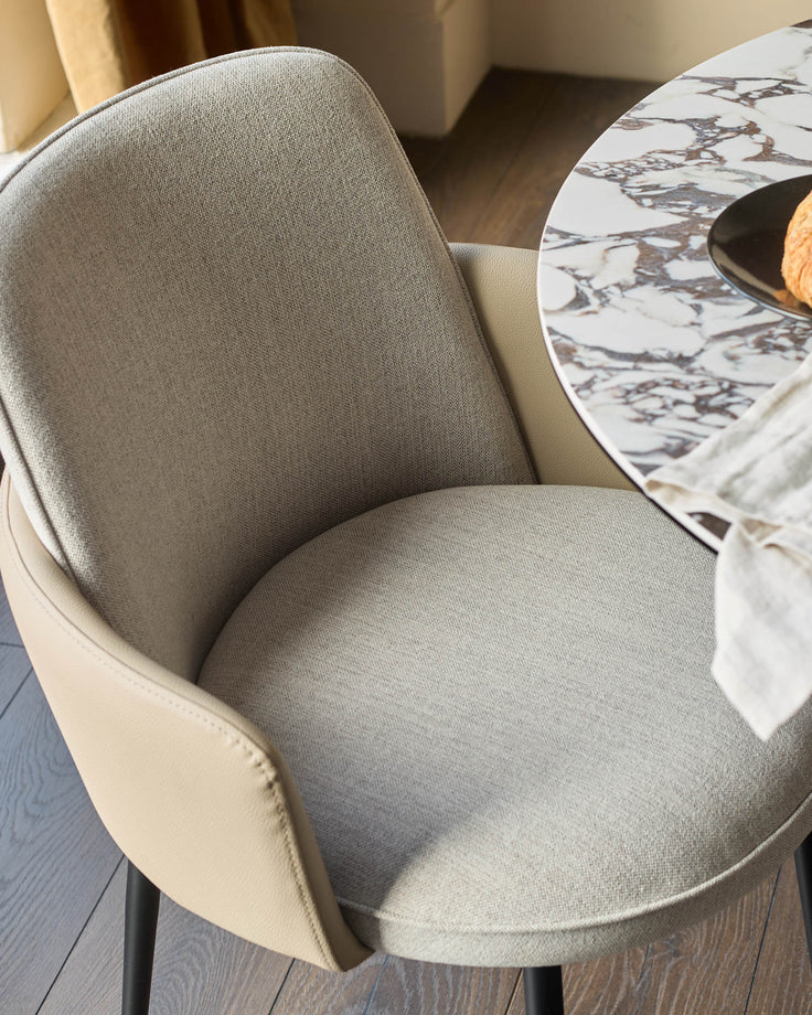 Wren dining chair in natural fabric and faux leather, shown at an angle next to a marble-top table with place setting.