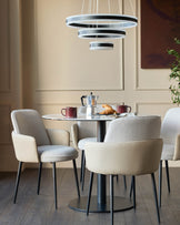 Wren dining chair in natural fabric and faux leather, shown in a modern dining setting with round table and pendant lights.