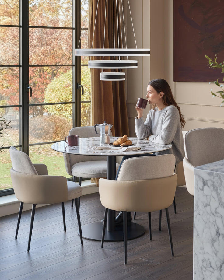 Wren dining chair in natural fabric, shown in modern dining setting with round table and autumn view through windows.